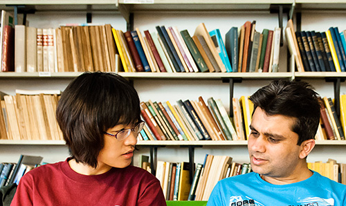 Two students sitting in front of shelves of colourful books