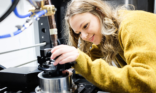 Yellow-jumpered student smiling while adjusting machinery
