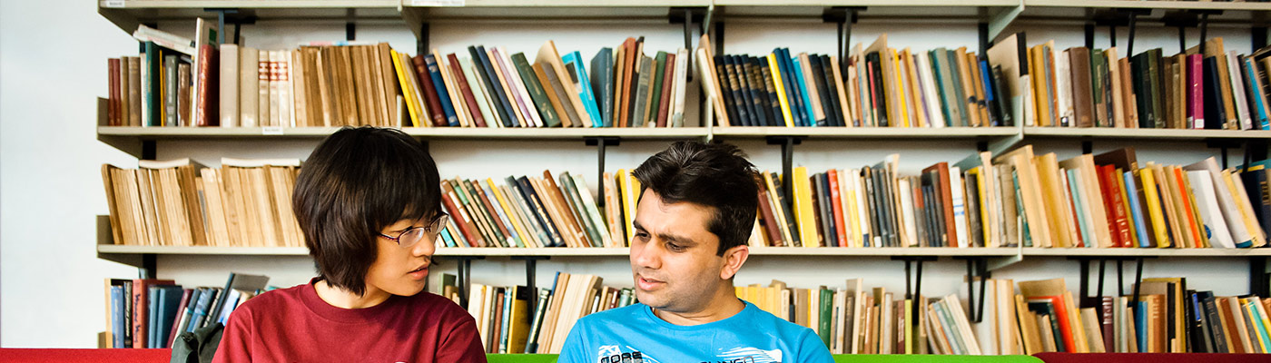 Two students sat in front of shelves of colourful books